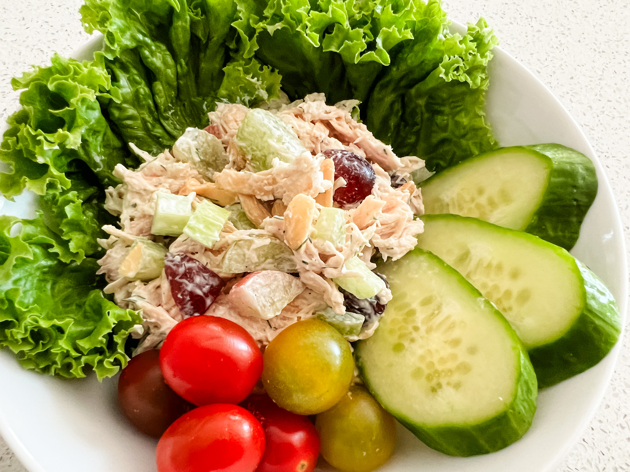 Bowl of chicken salad with lettuce, cherry tomatoes and sliced cucumbers