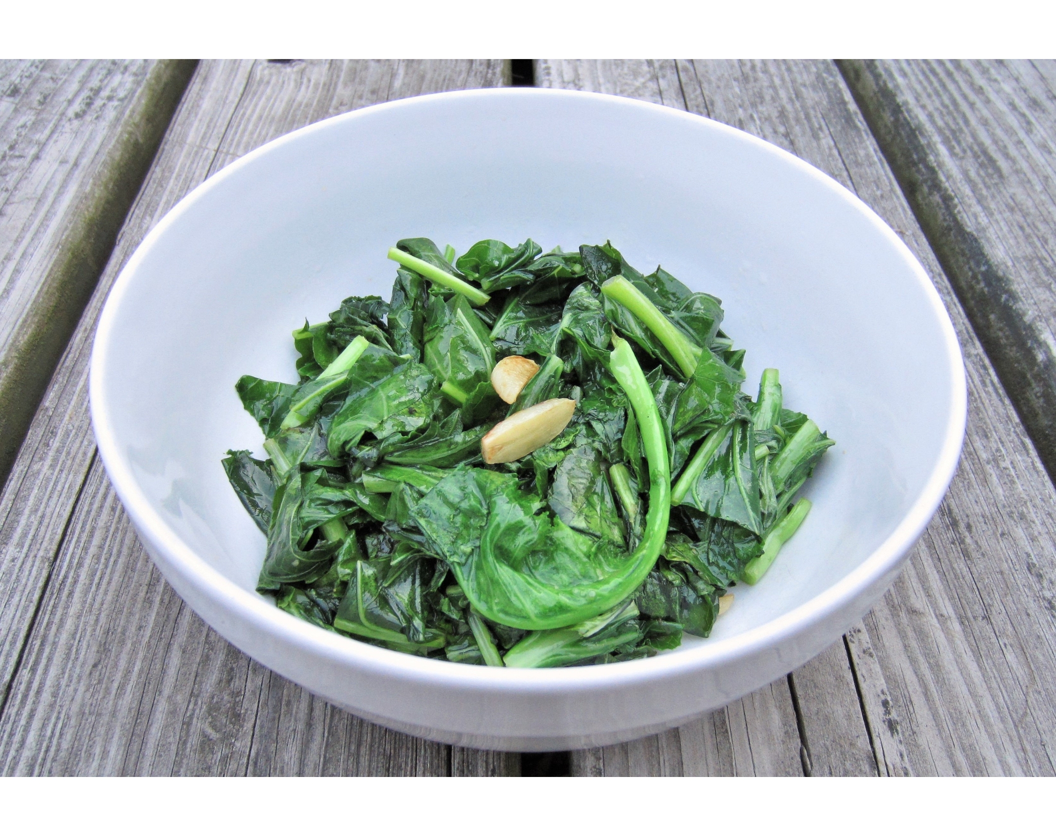 sautéed collard greens in a white bowl on a wooden table 